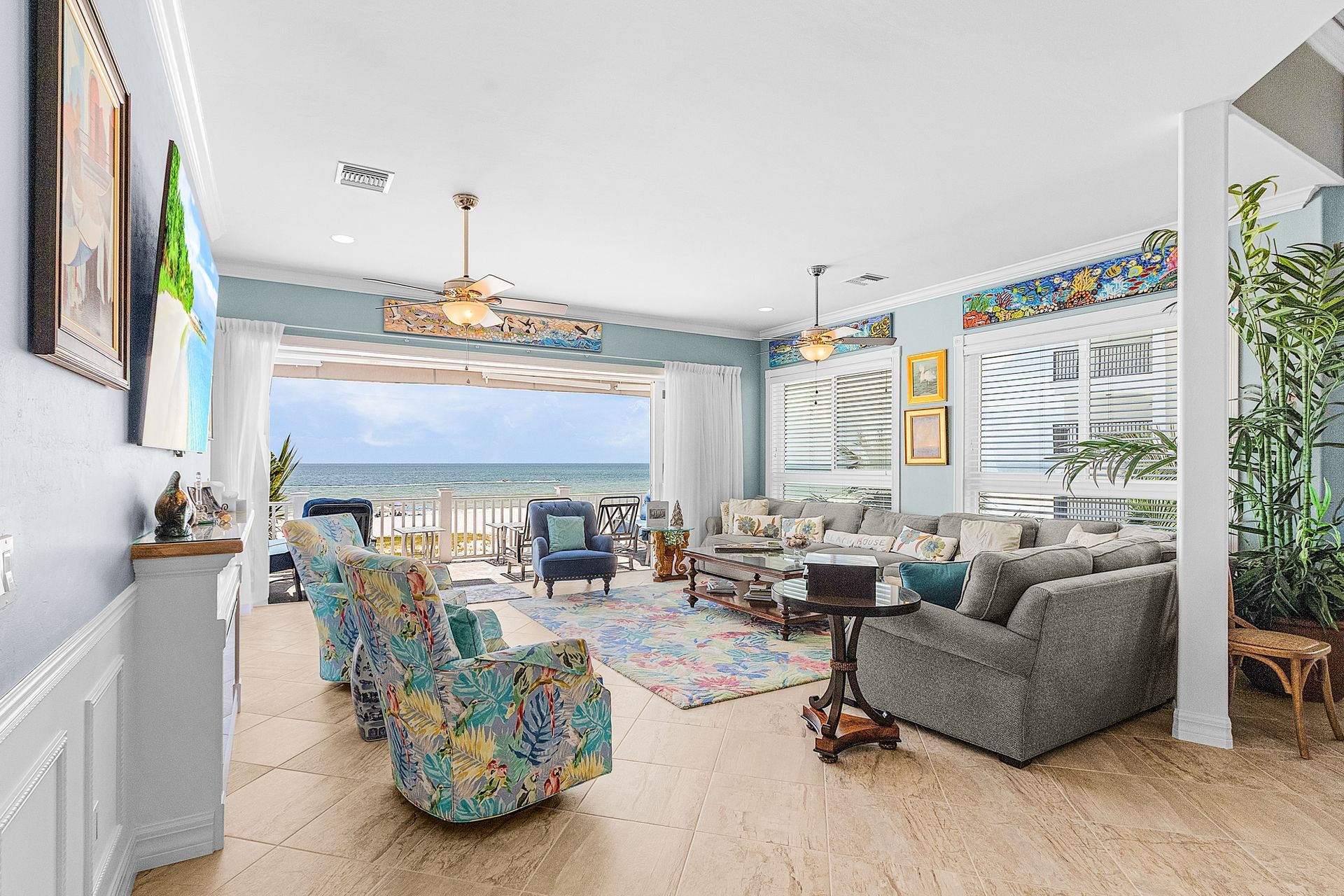 Bright coastal living room with ocean view, colorful chairs, gray sofa, and large sliding glass doors