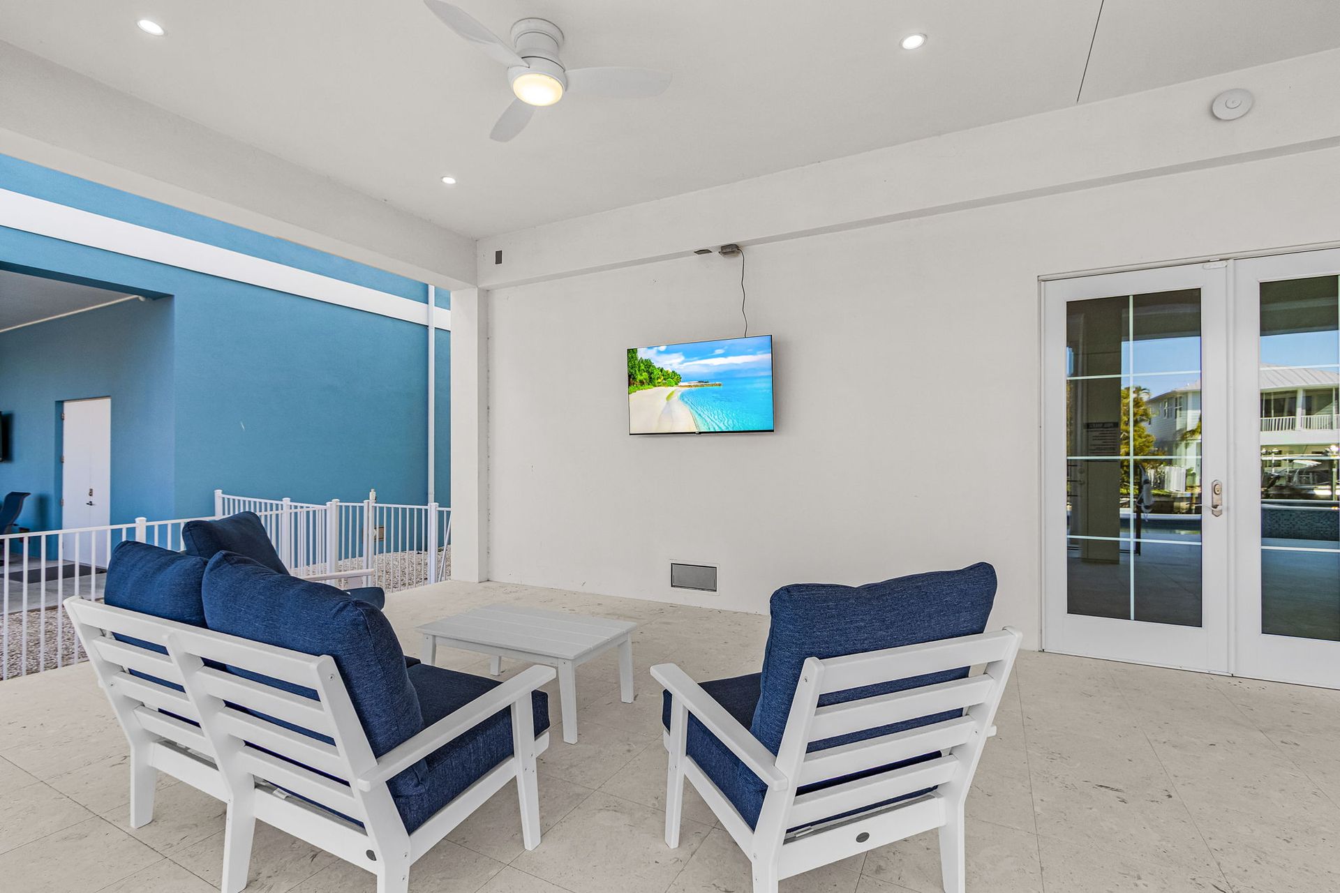 Patio with blue seating, white table, and TV on a white wall.