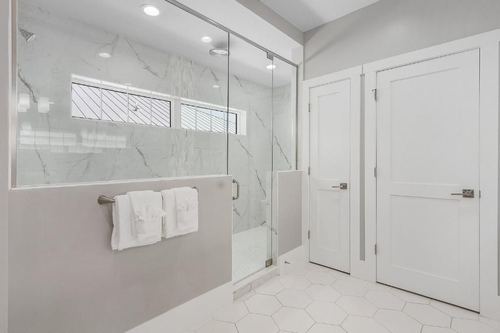 Modern white bathroom with glass shower, two white doors, and hexagon tile floor.
