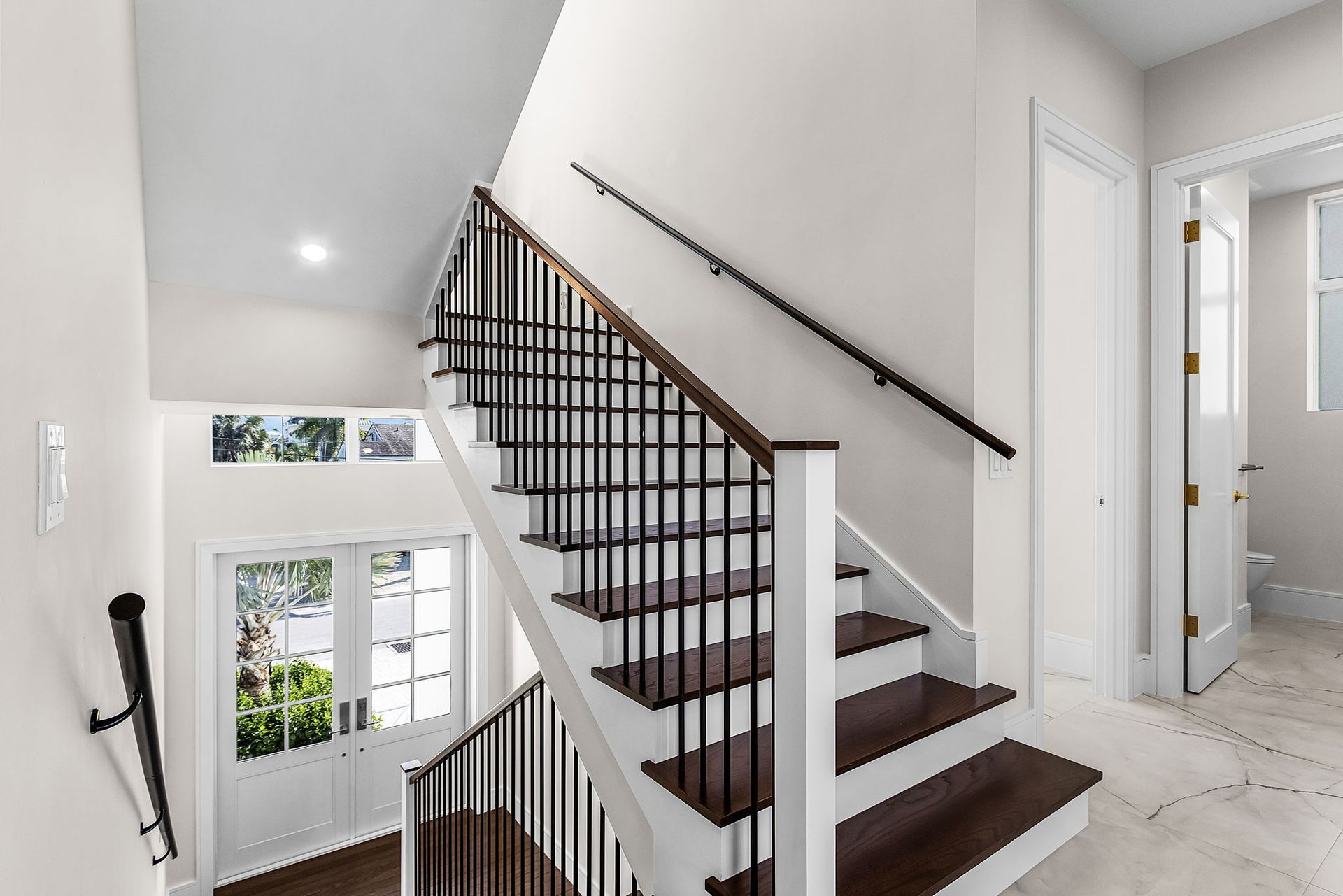 Staircase with dark wood steps and black railing, white walls and trim, natural light from windows.