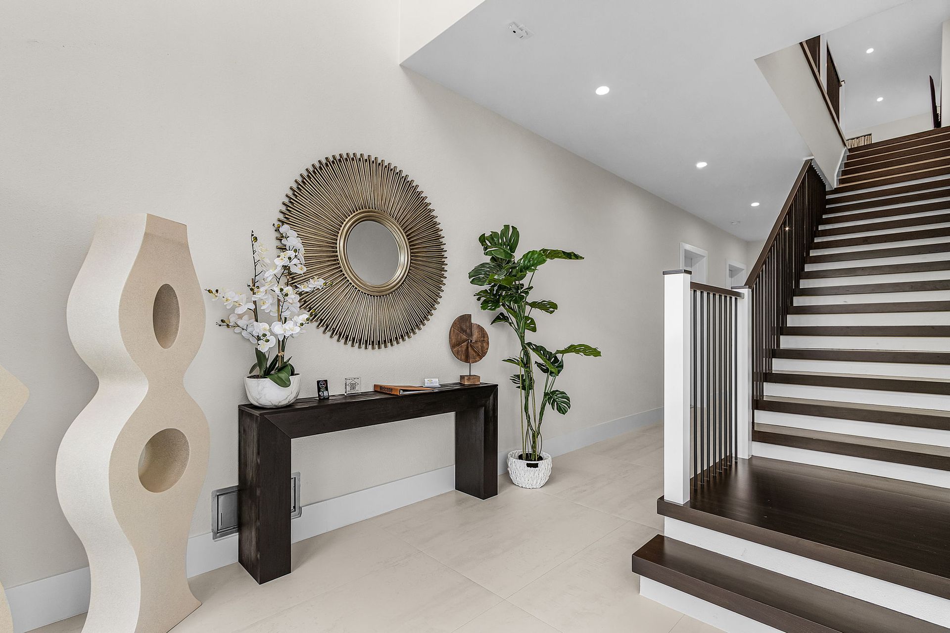 Entryway with a staircase, console table, large mirror, and decorative sculptures.