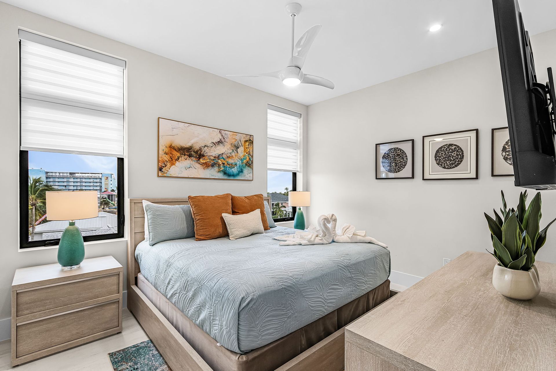 Bedroom with a king bed, art, two windows, two nightstands, and a TV.