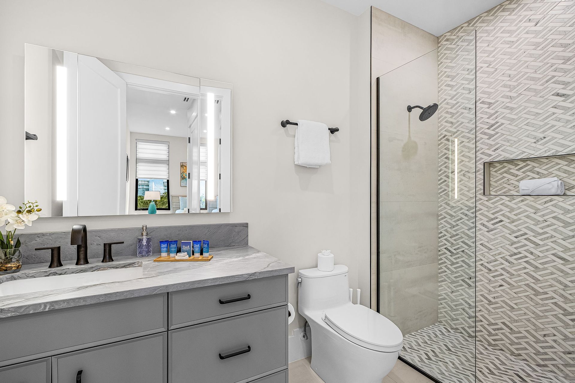 Modern bathroom with gray vanity, white toilet, and tiled shower.