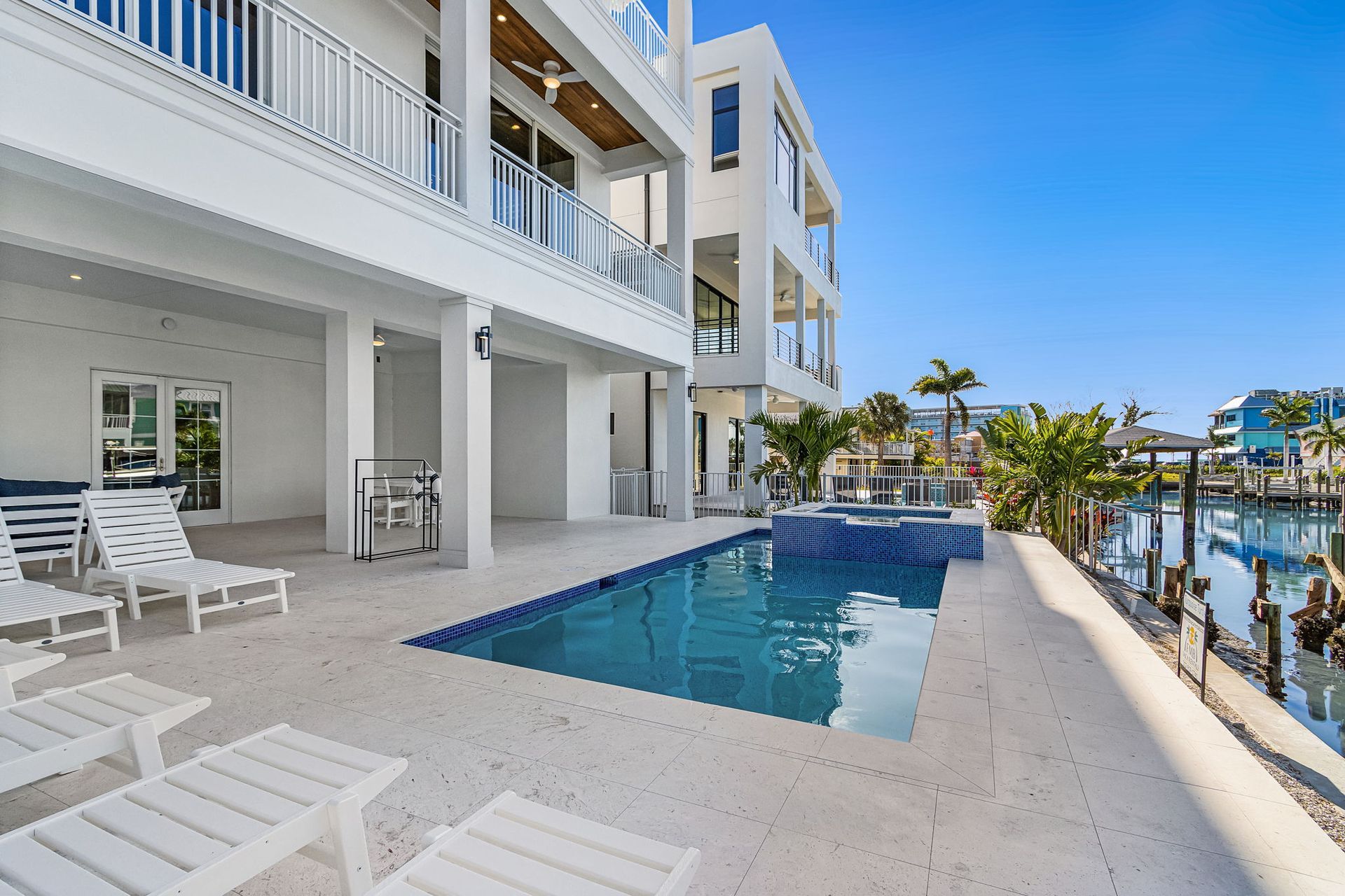 Modern white waterfront home with pool and dock on a sunny day.