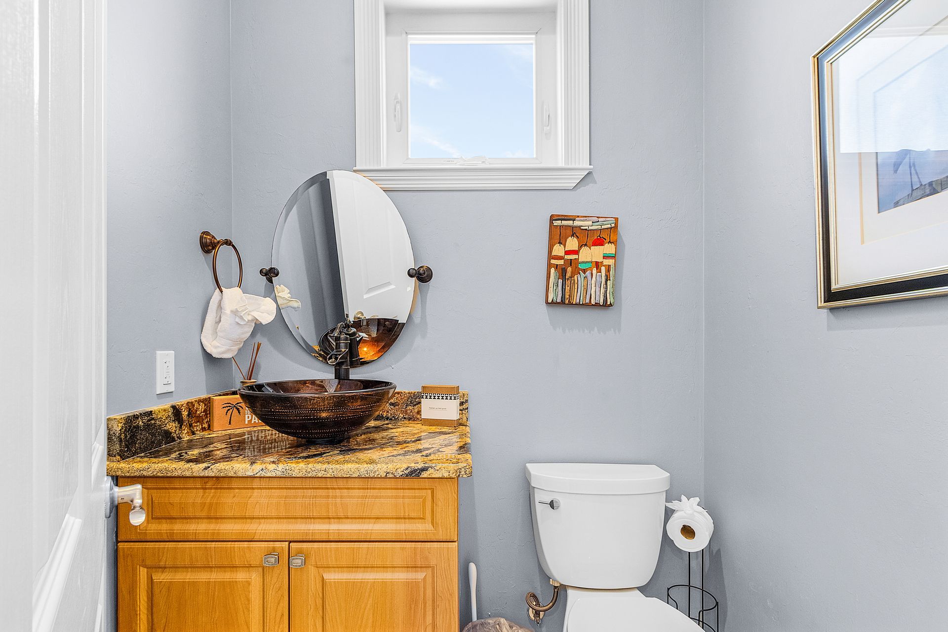 Small bathroom with granite vanity, round mirror, toilet, and light gray walls.