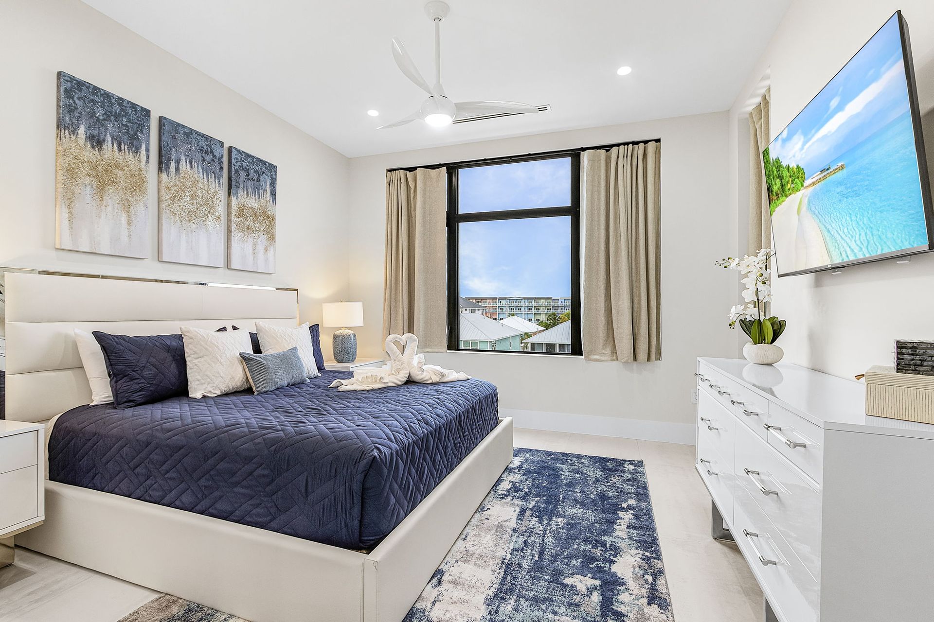 Bedroom with a king-size bed, blue and white decor, large window, and wall-mounted TV.
