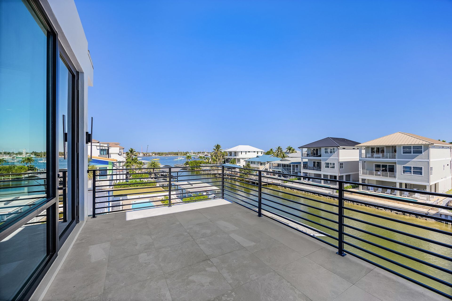 Balcony view overlooking a canal with houses, blue sky, and black railings.