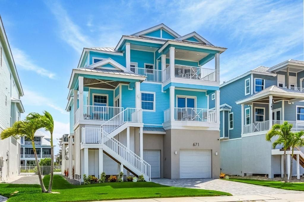 Three-story turquoise beach house with balconies, white trim, and a garage under a bright blue sky.