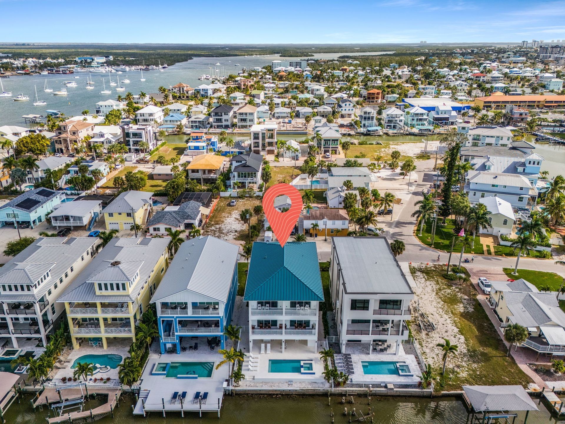 Aerial view of waterfront homes with pools, docks, and a marked location.