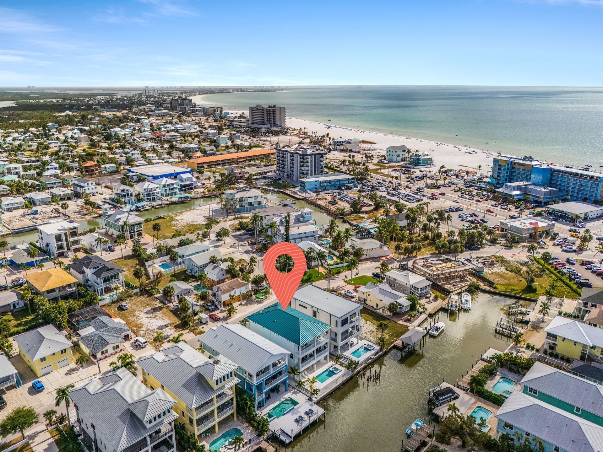 Aerial view of coastal buildings with a beach and ocean in the background, a location marker is in the center.