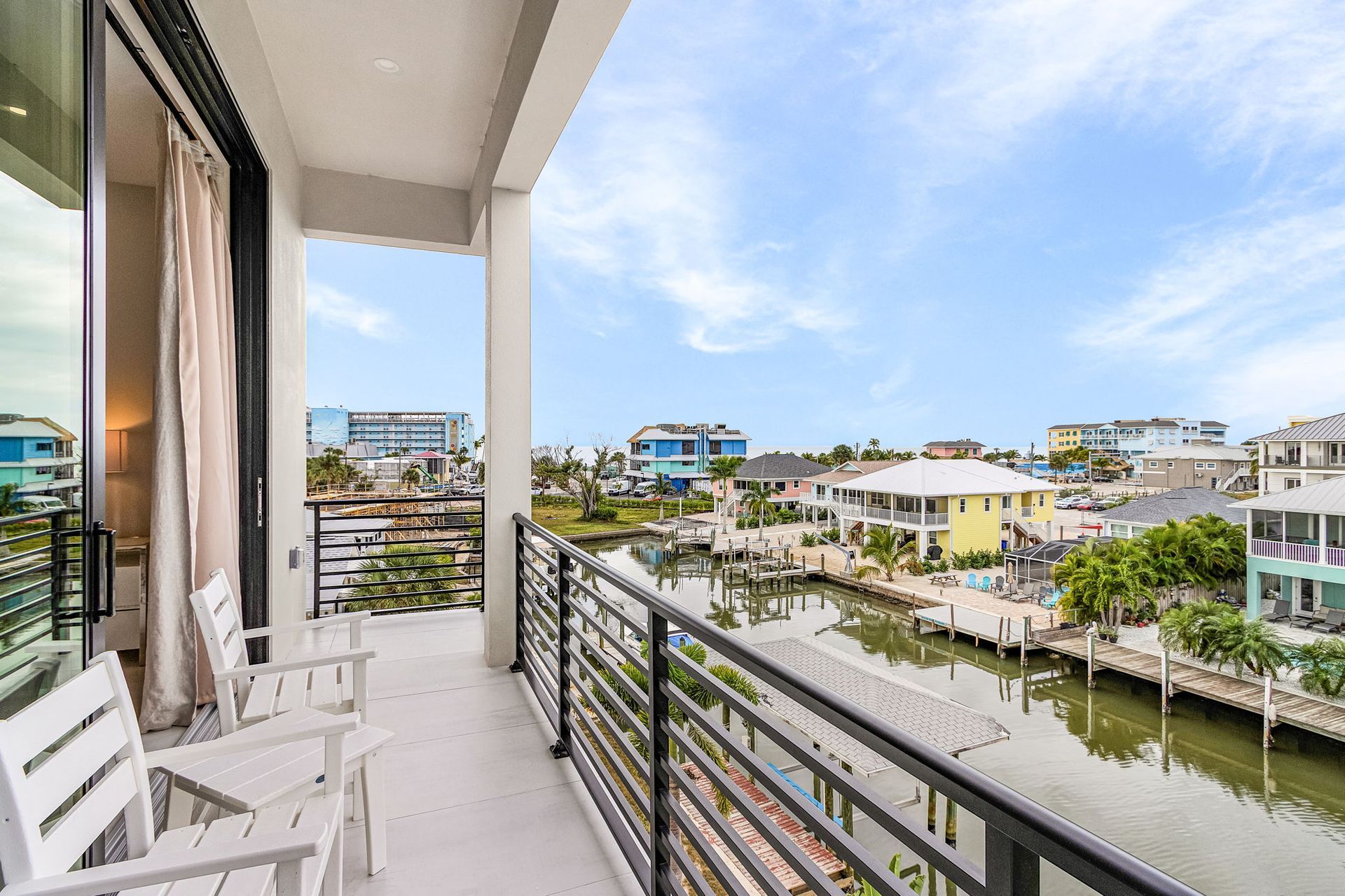 Balcony overlooking canal and waterfront homes, blue sky. White chairs and metal railing.