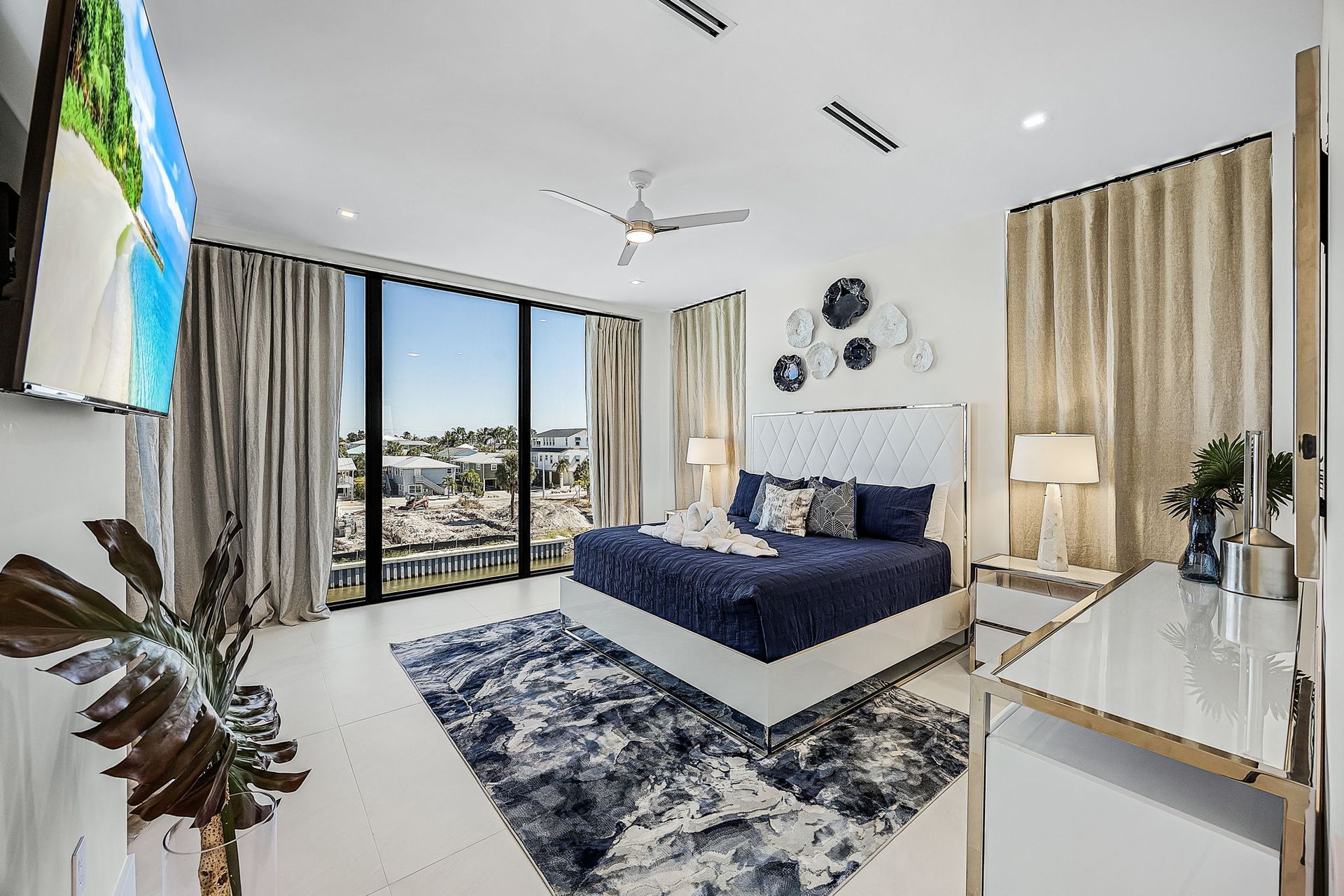 Modern bedroom with a bed, large windows, and city view, with blue and white decor.