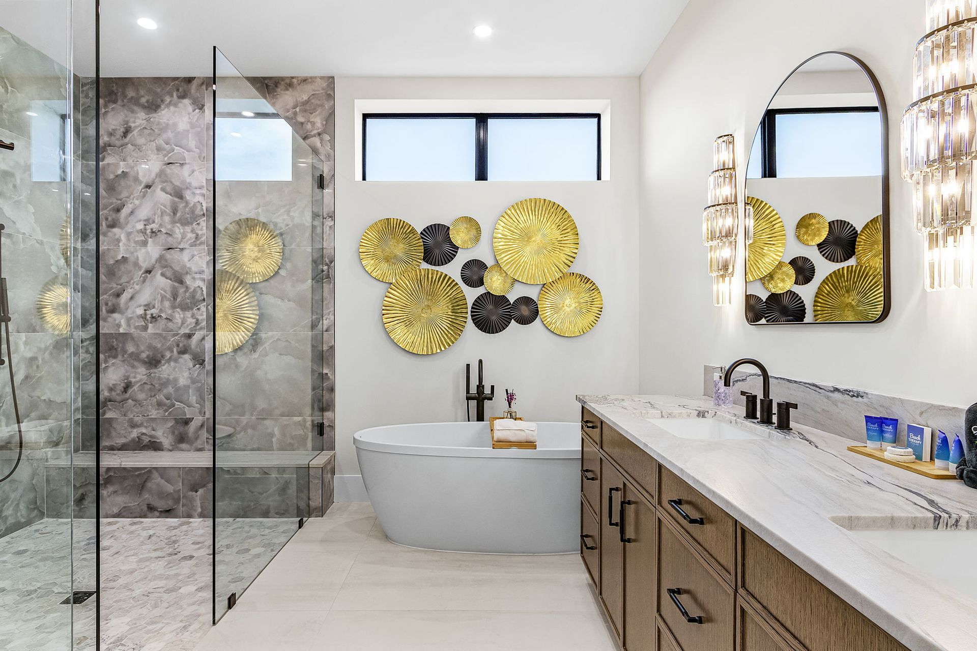 Modern bathroom with a glass shower, soaking tub, double vanity, gold wall decor.