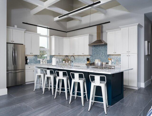 Modern kitchen with white cabinets, blue backsplash, dark blue island, stainless steel appliances, and white stools.