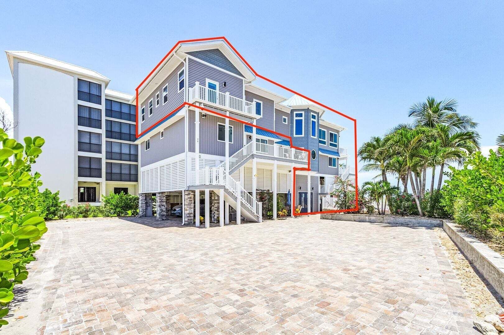 Modern white multi-story building with red roof trim and a wide sandy driveway under clear skies
