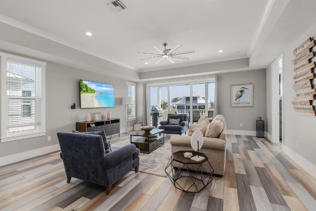 Spacious living room with gray and wood tones. Blue armchair, sofa, and large TV. Large windows with a view.