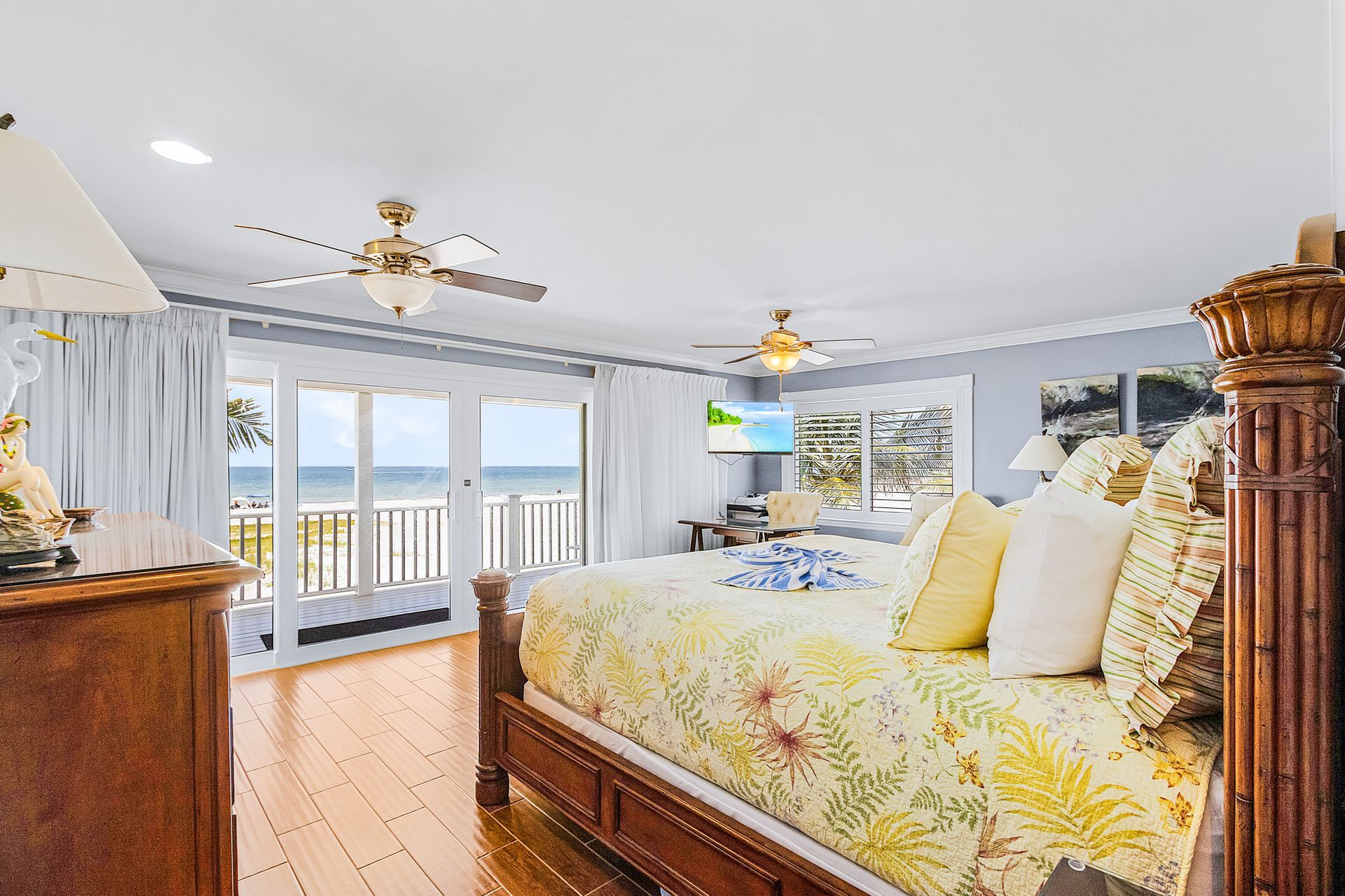 Bright bedroom with floral bedspread, wood furniture, and balcony doors overlooking the water