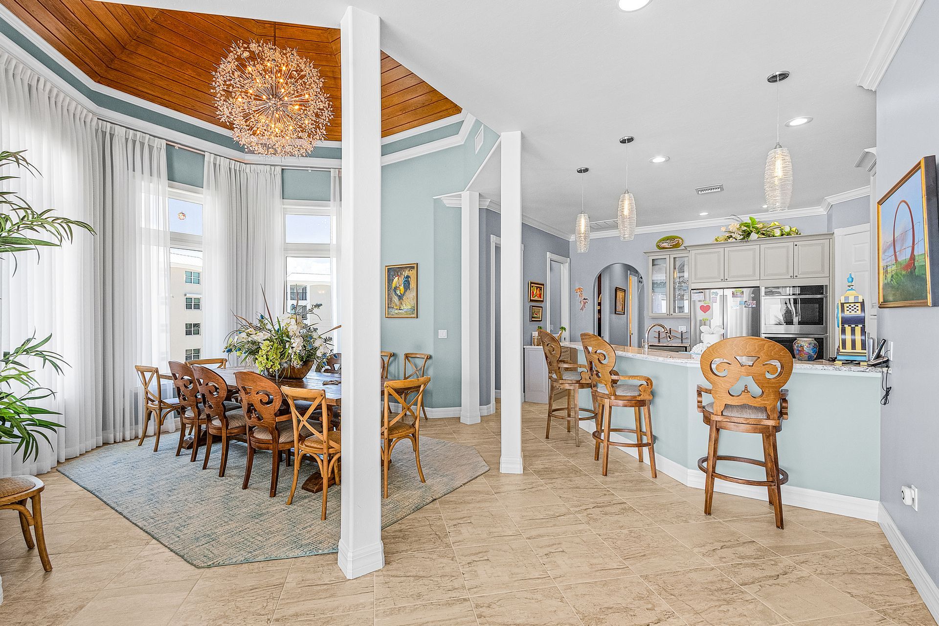 Bright, airy dining room with wicker chairs, blue accents, tall windows, and a tiled floor