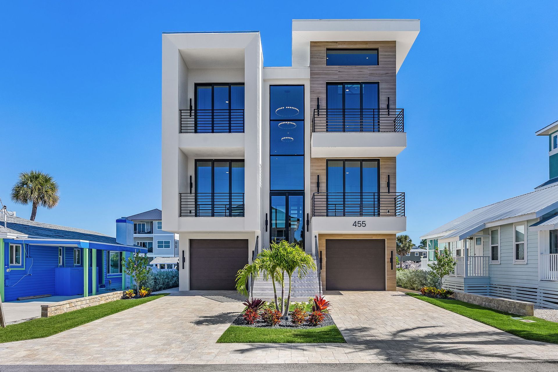Modern three-story white house with blue windows and brown garage doors on a sunny day.