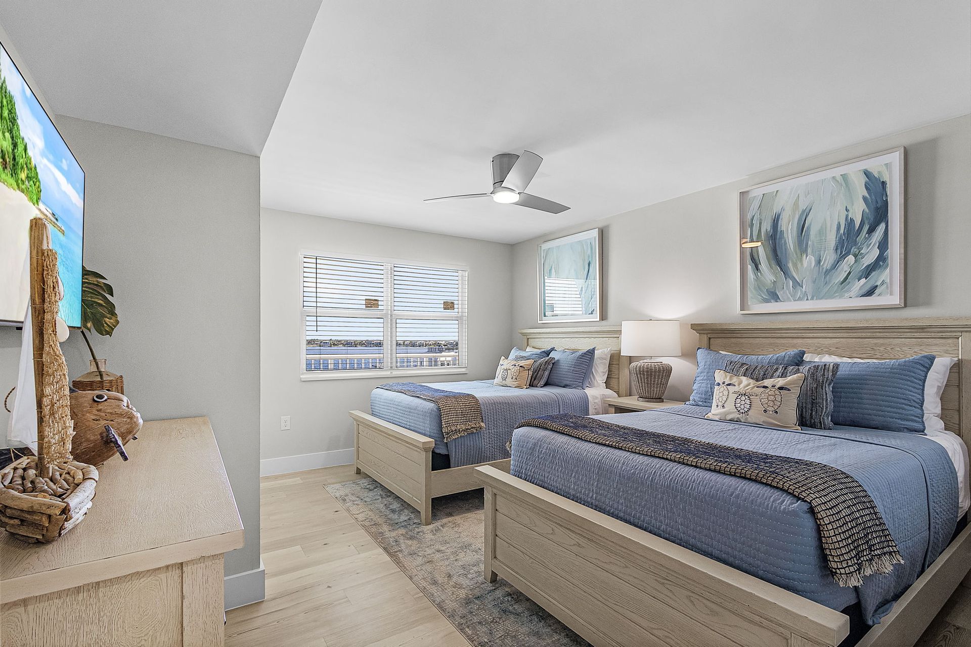 Bedroom with two beds, light blue bedding, pale wood furniture, and a window.