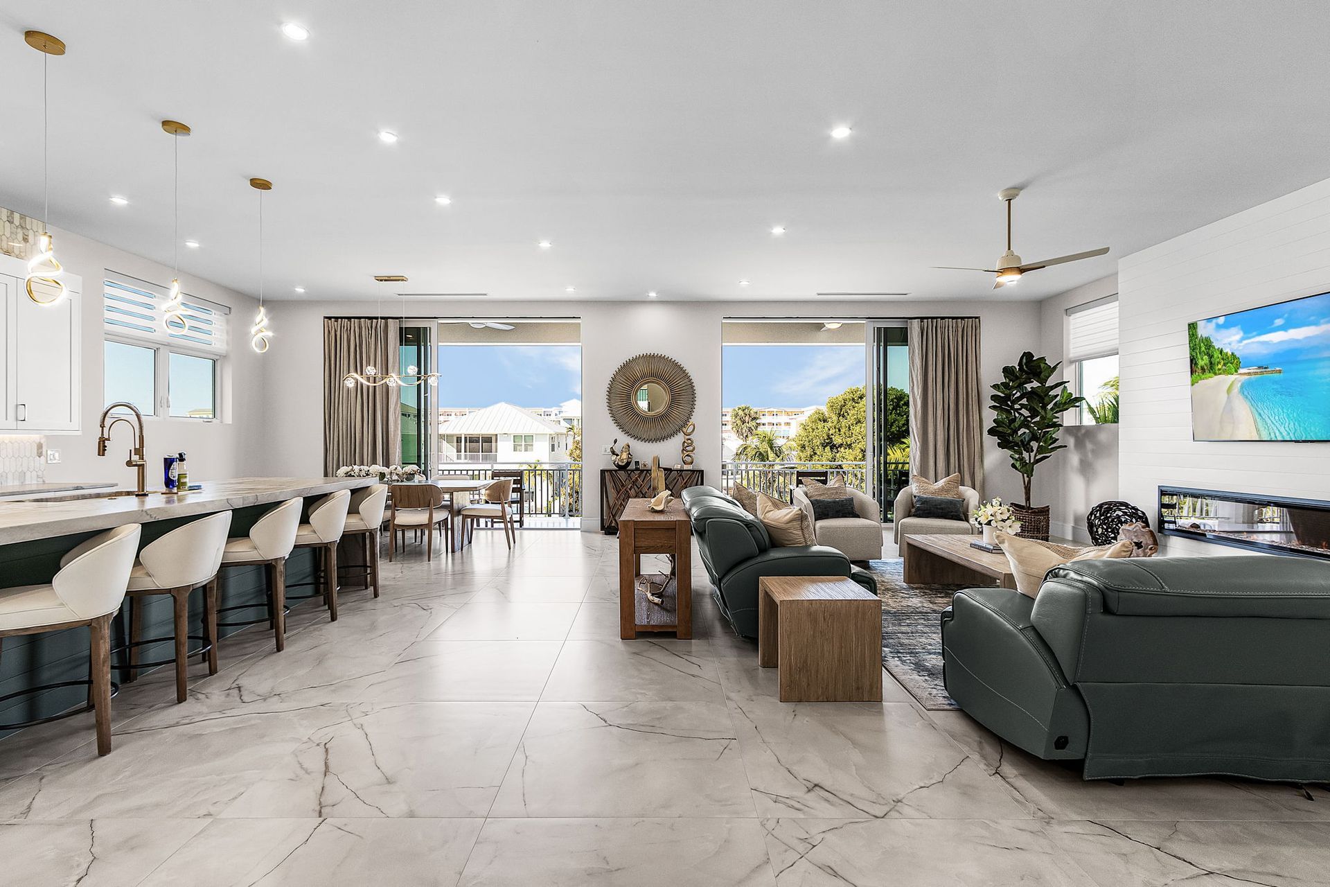 Spacious, modern living room with open kitchen, marble floors, and large windows leading to an outdoor view.