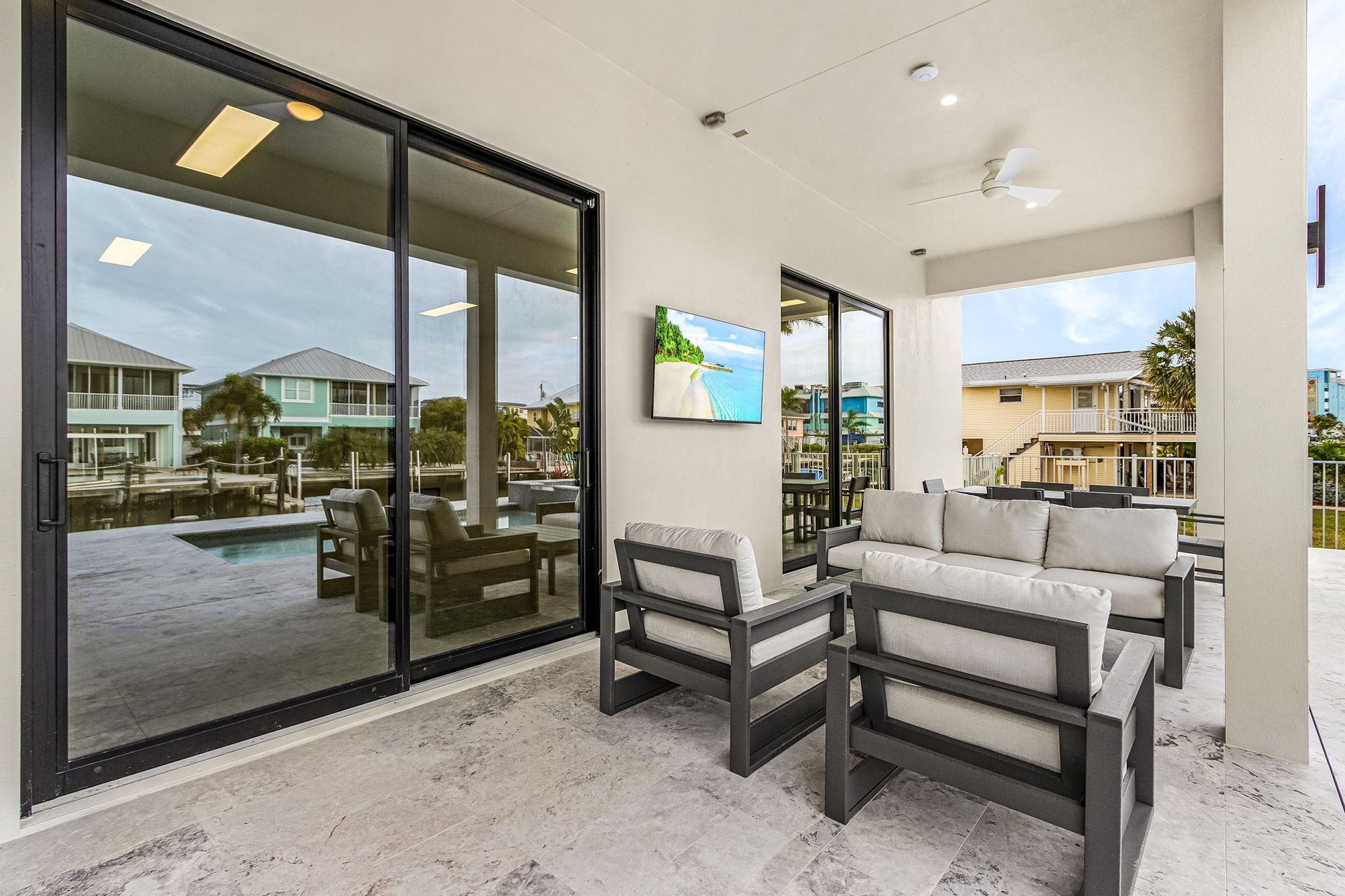 Patio with outdoor seating, sliding glass doors, and a TV. Buildings and water are visible.