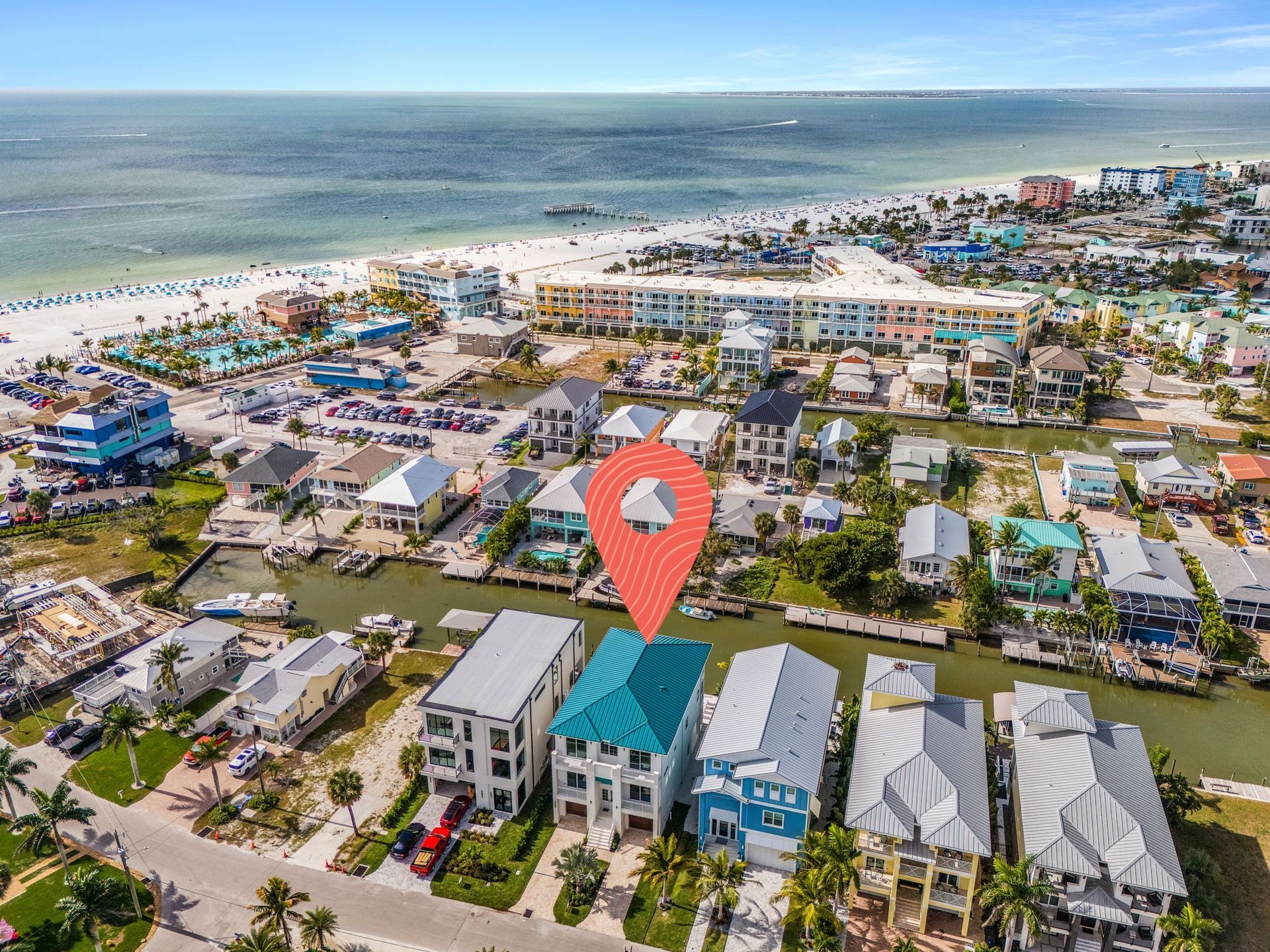 Aerial view of waterfront houses with a location pin, beach in the background.