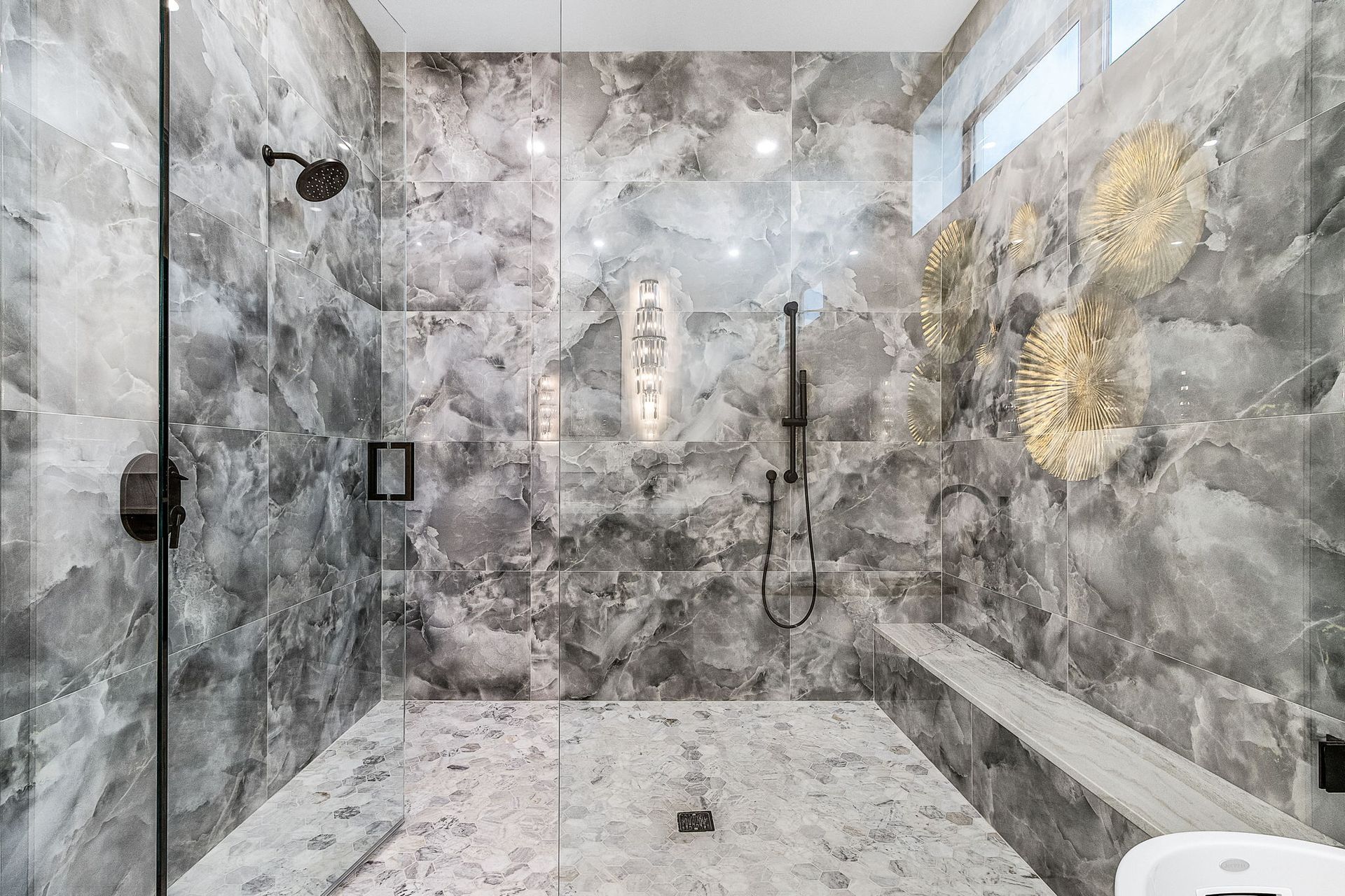 A luxurious gray marble shower with glass door and black fixtures.