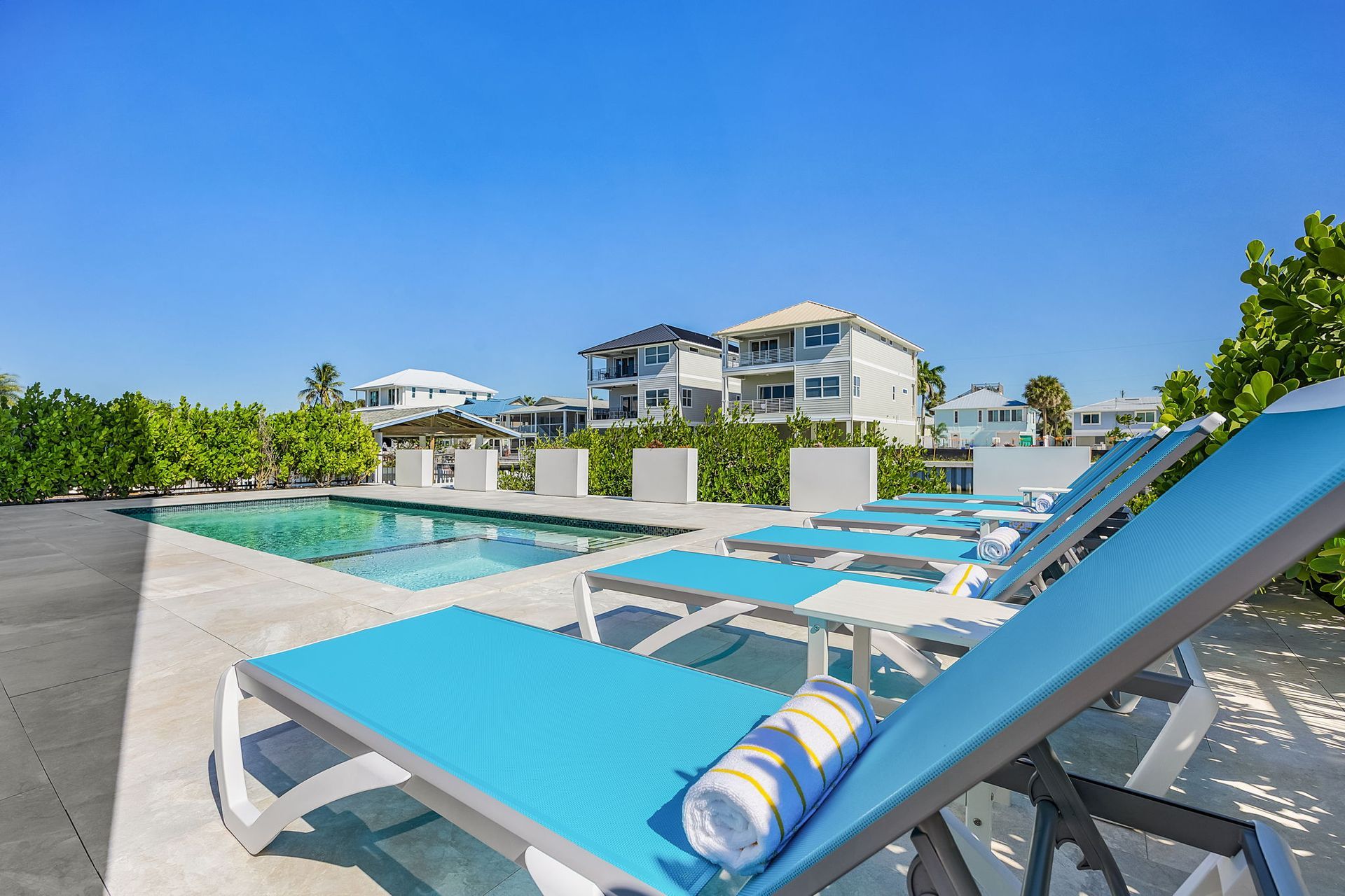 Poolside scene with blue lounge chairs, pool, and multi-story building under a clear sky.