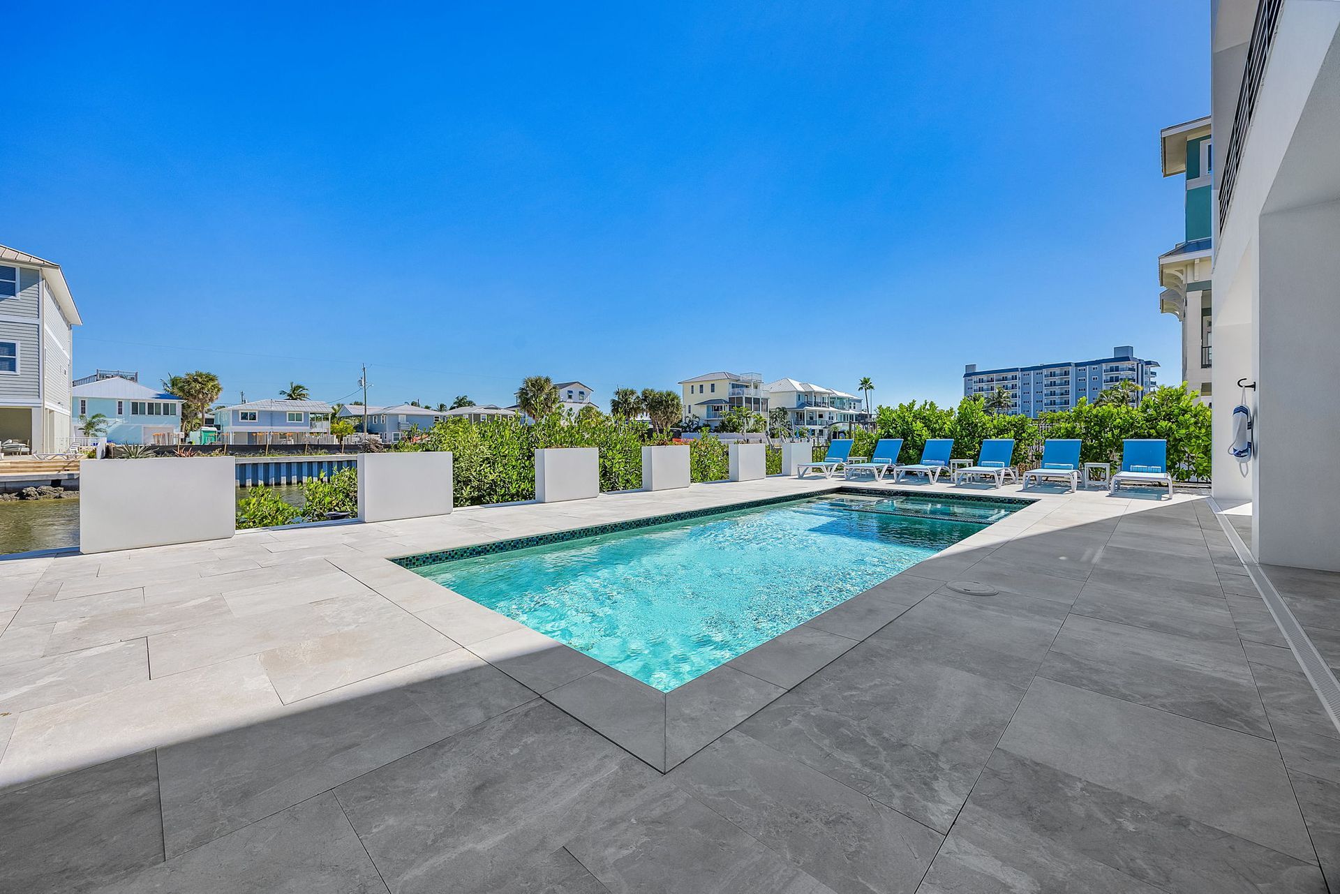 Swimming pool next to a waterway; blue water, sunny day, lounge chairs, buildings in background.