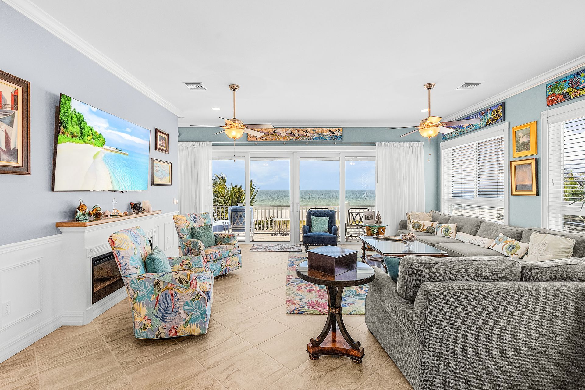Bright seaside living room with colorful chairs, gray sofa, ocean-view windows, and large wall art