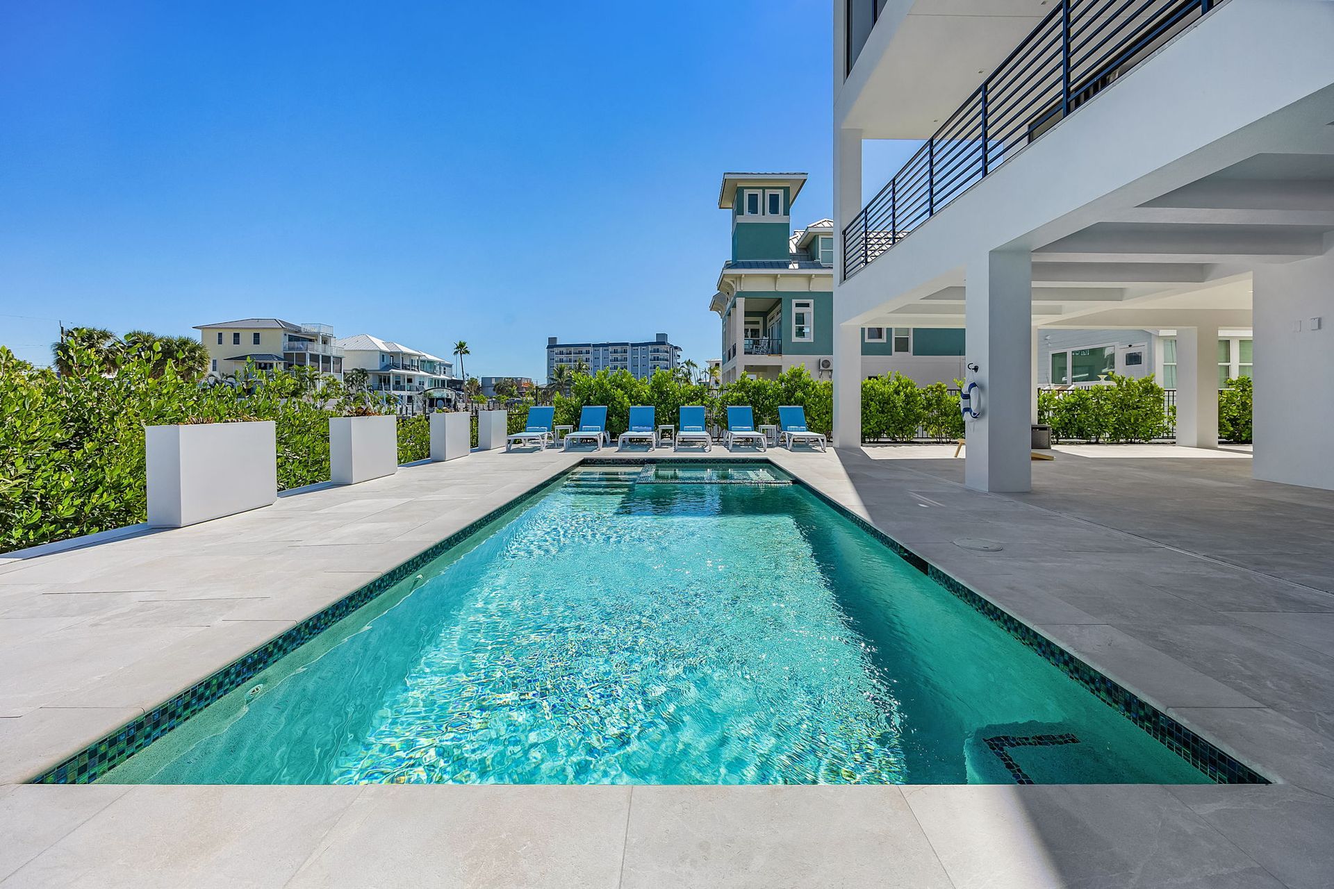 Pool with turquoise water, lounge chairs, and building on a sunny day.