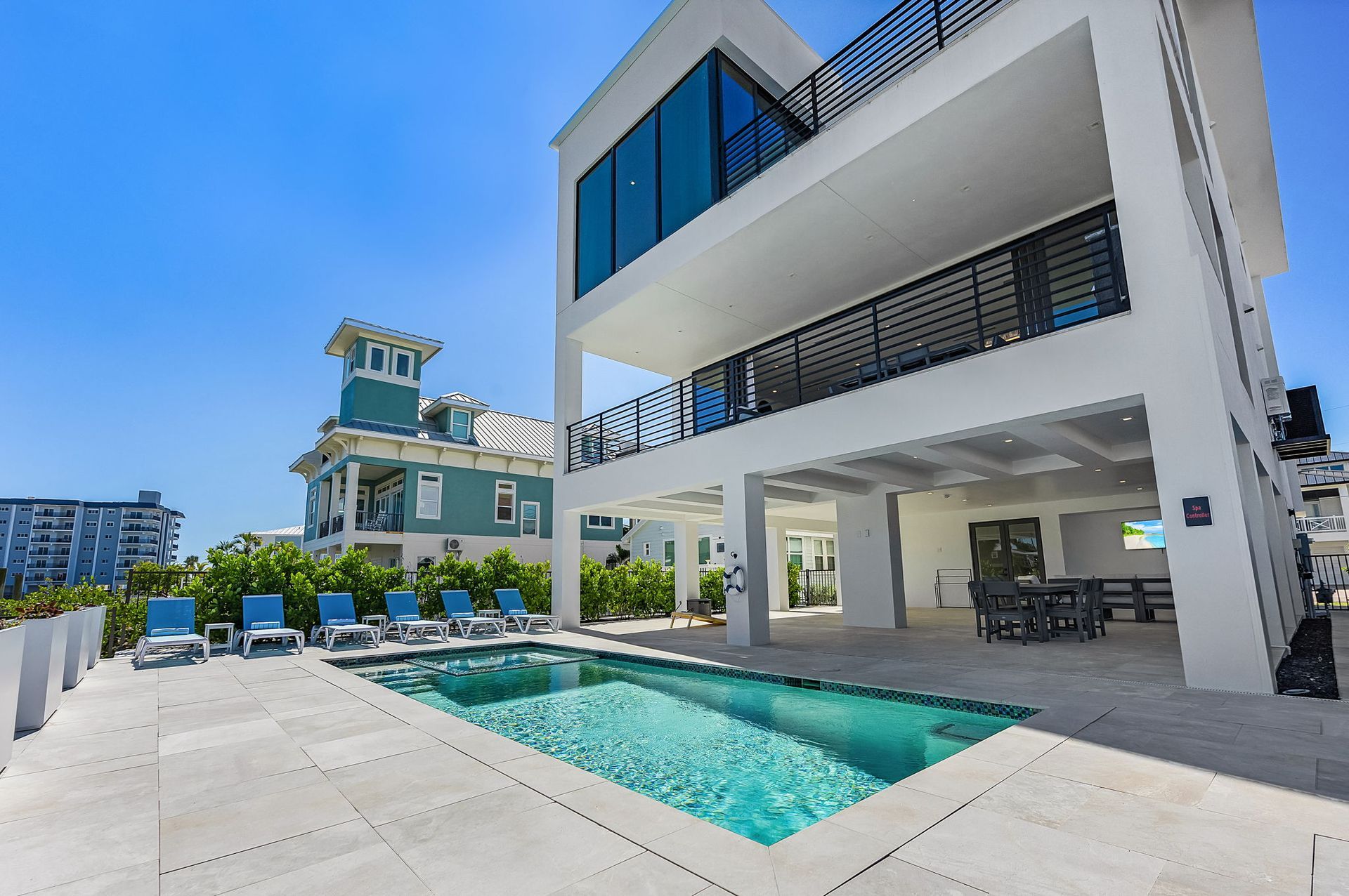 Modern white beach house with a pool, patio, and ocean view on a sunny day.