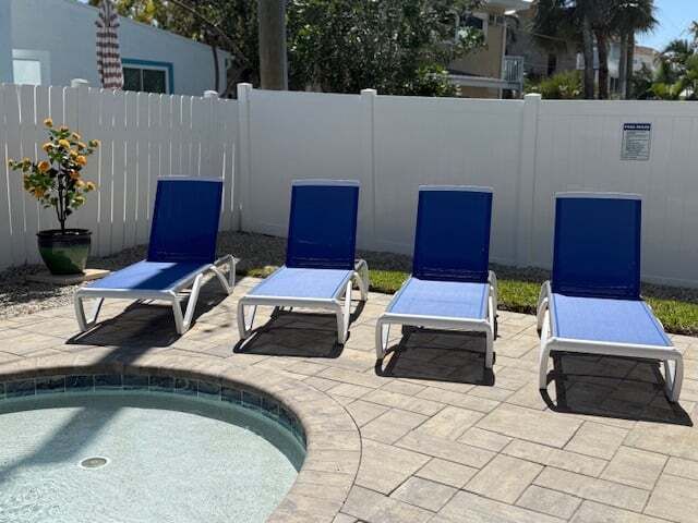 Four blue and white lounge chairs beside a pool, against a white fence.