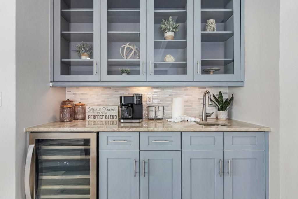 Blue-painted kitchen bar with glass-front cabinets, wine fridge, coffee maker, and sink.