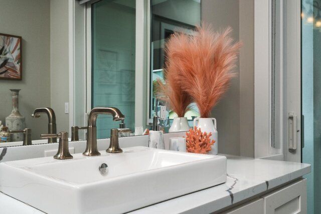 Bathroom vanity with white sink, bronze faucet, and coral-colored decorative pampas grass.