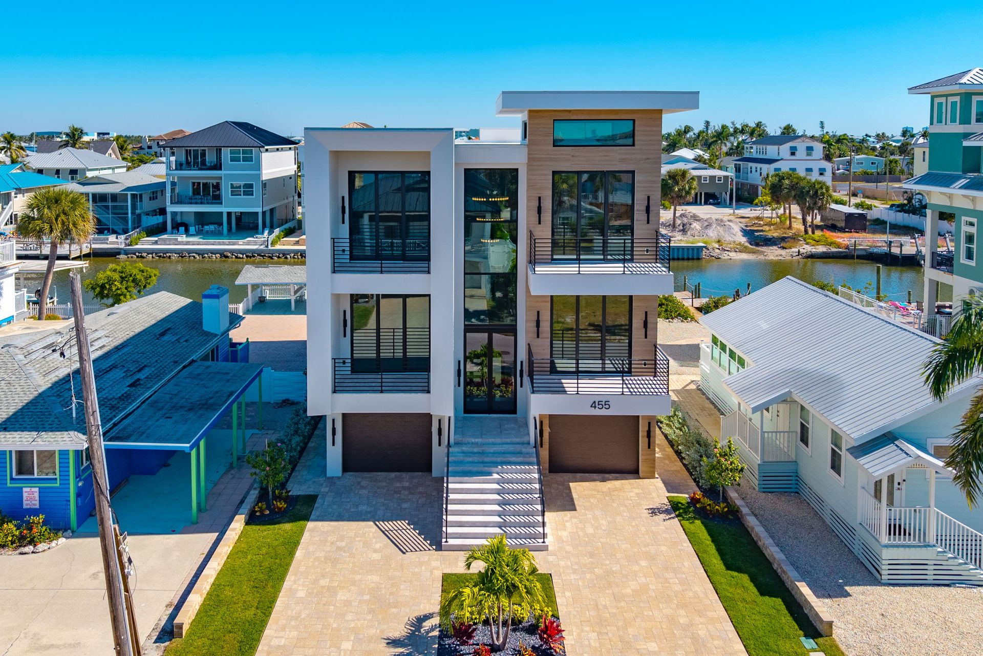 Modern, multi-story waterfront home with glass walls, concrete exterior, and blue sky.