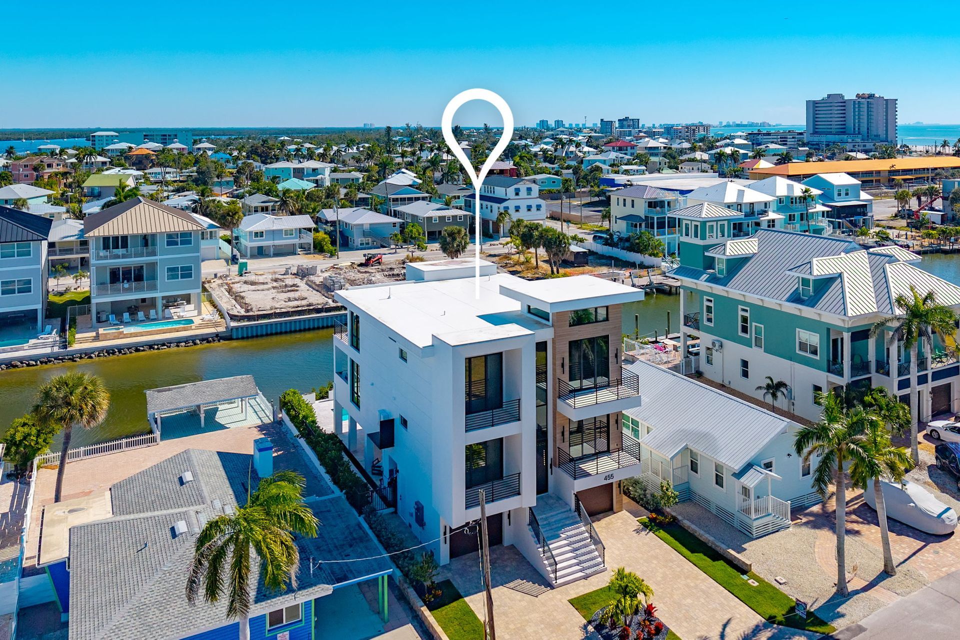 Aerial view of a modern white house with a canal and cityscape in the background.