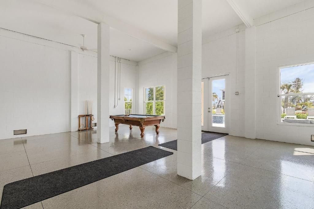 Large white room with glossy floor, pool table, pillars, and windows.