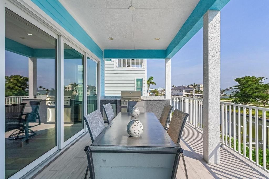 Outdoor dining area with table and chairs on a balcony, overlooking a waterfront and other buildings.