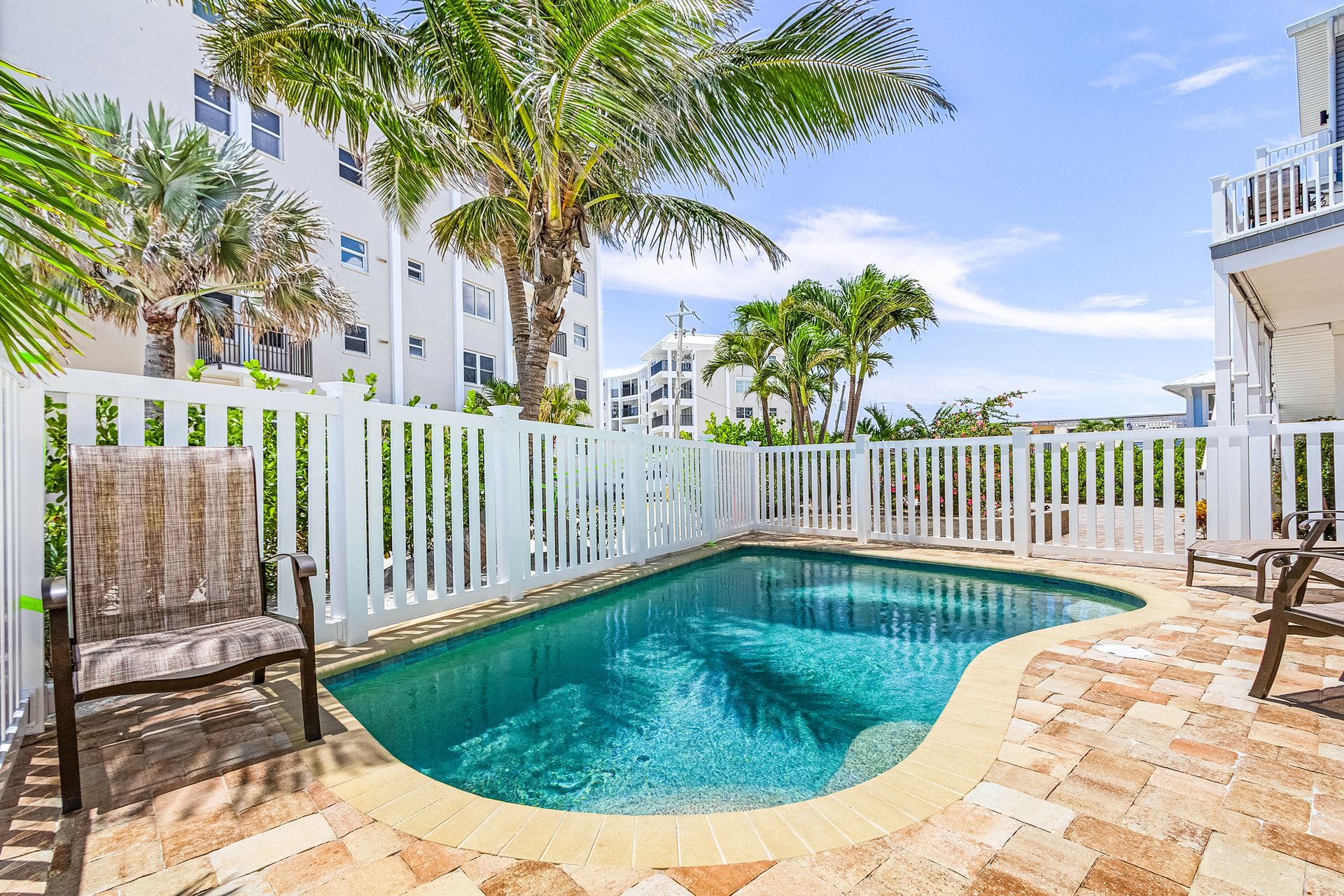 Small turquoise pool in a sunny tropical courtyard with palm trees and white fence