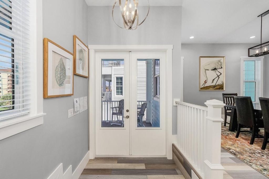 Entryway with double doors, art, and staircase leading to a dining area. Gray walls, wood-look flooring.