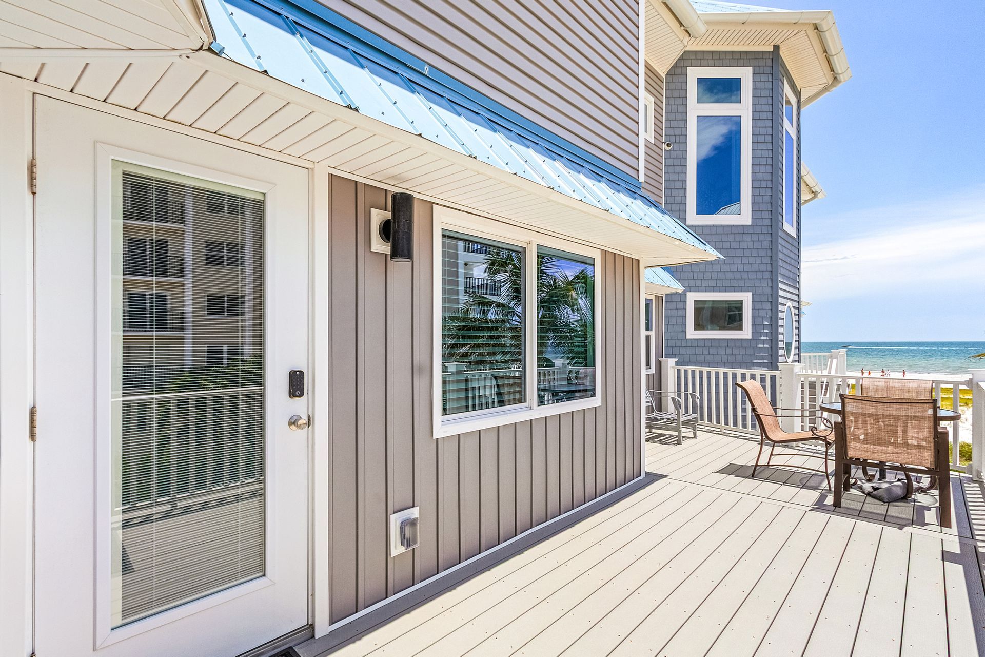 Oceanfront deck beside a beige house with white trim, patio furniture, and a view of the sea