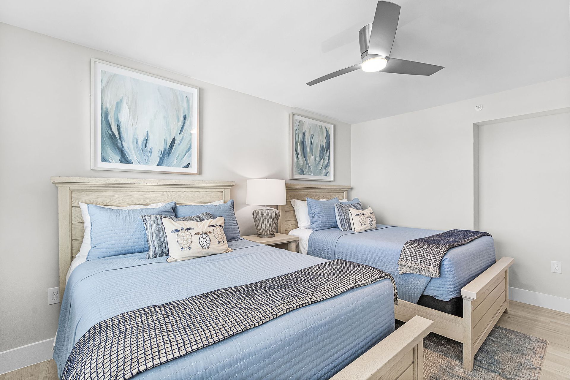 Bedroom with two beds, blue and white decor, artwork on the walls, and a ceiling fan.
