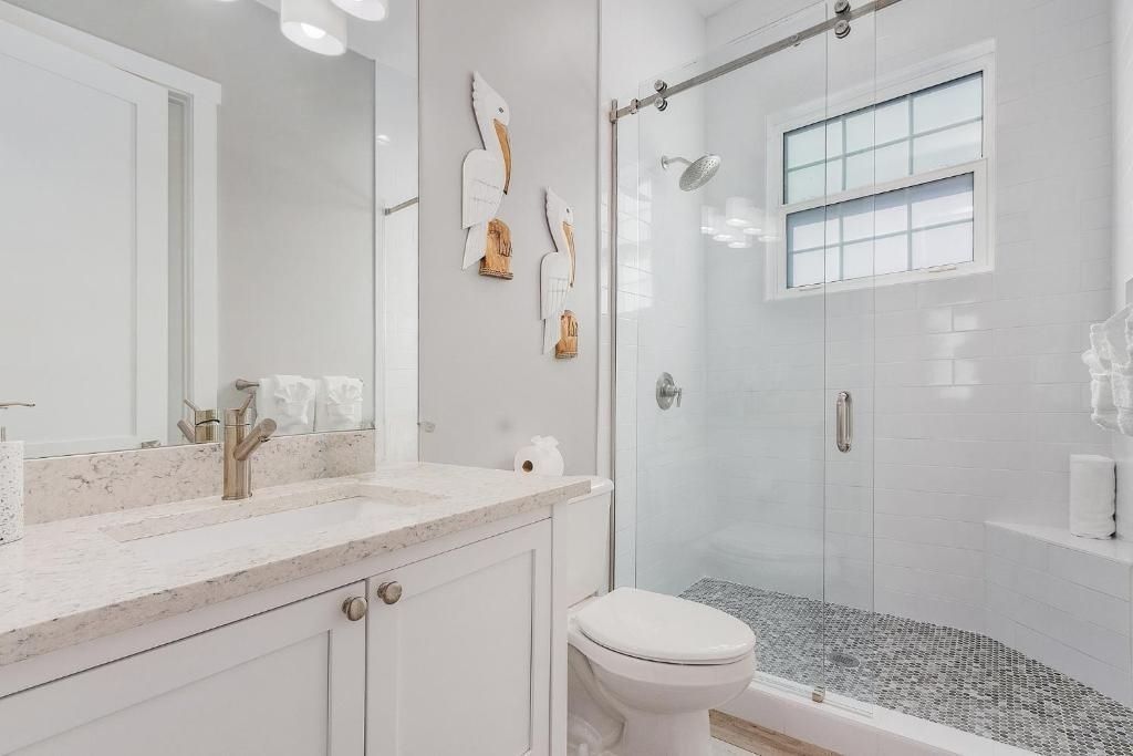 White bathroom with a shower, toilet, and vanity. Gray pebbles line the shower floor.