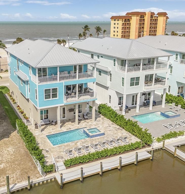 Two-story beach houses with pools, light blue and white exteriors, near the ocean.