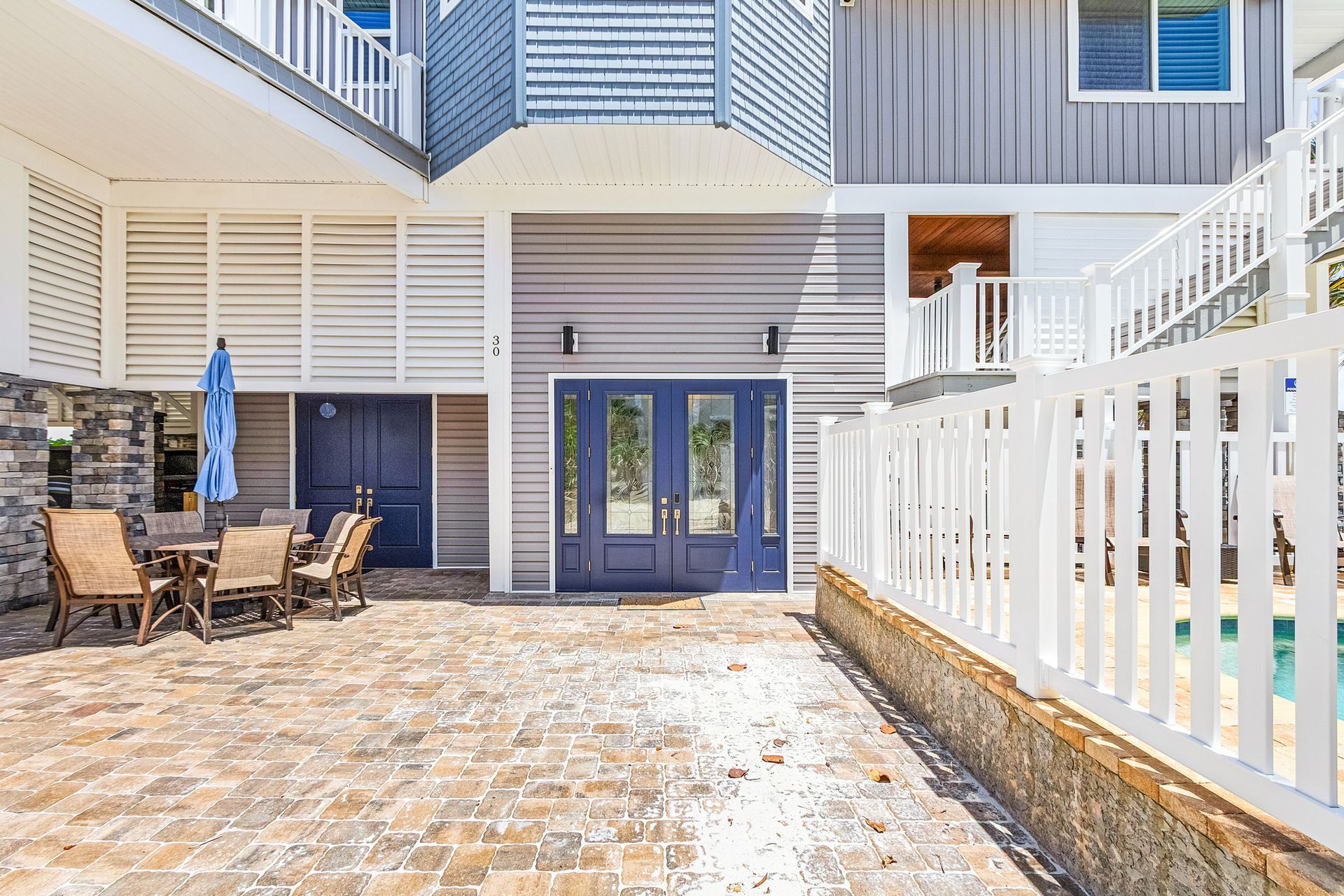 Courtyard patio with stone pavers, blue double doors, and white railings beside a building