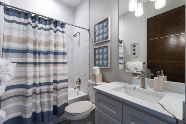 Bathroom with blue and beige striped shower curtain, white sink and vanity, and seashell art.