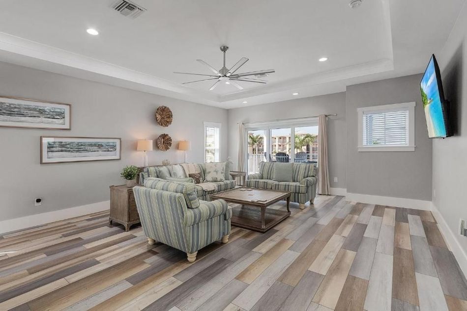Living room with patterned hardwood floor, light gray walls, striped armchairs, and a large TV.
