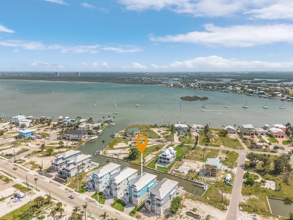 Aerial view of waterfront homes with canal access, blue sky, and a location marker.